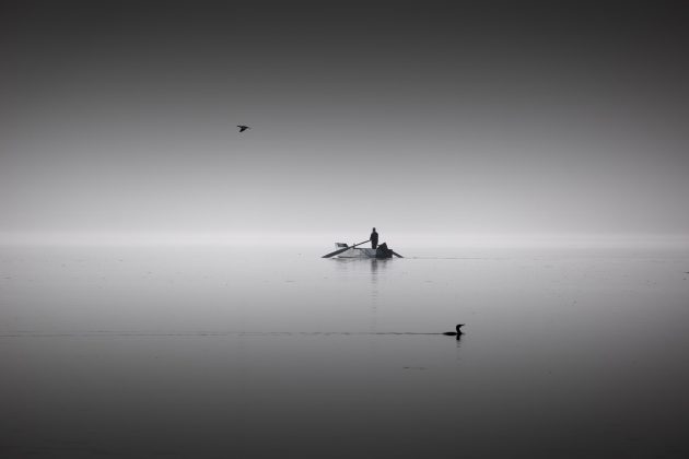 Distant person standing in fishing boat in open calm waters