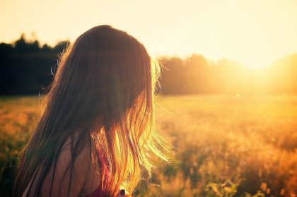 Woman in a field looking at the sun setting.