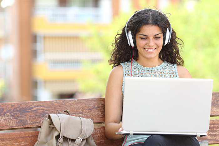 Woman with headphones sitting on park bench using her laptop