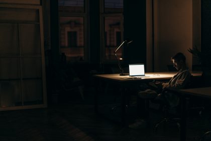 Person sitting as desk in a dark room illuminated by a laptop screen