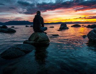 Man sitting on rock in lake looking at the sunset