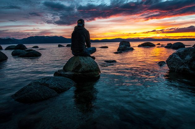 Man sitting on rock in lake looking at the sunset