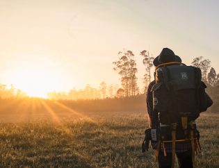 Hiker with backpack looking across field to setting sut