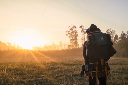 Hiker with backpack looking across field to setting sut