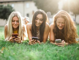 Three woman laying on grass using phones