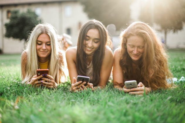 Three woman laying on grass using phones